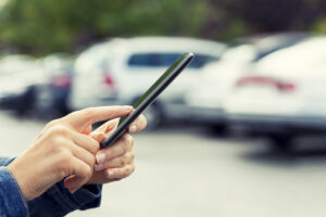 Female's hand looking for her car with smartphone API in a parking lot. Blur Cars background.